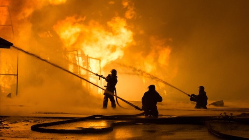 Firefighters spraying water onto a blazing building at night.