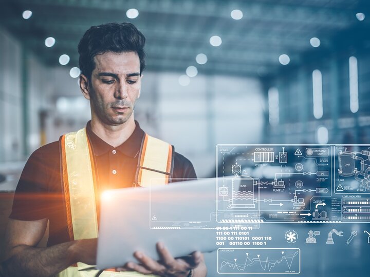 Worker in a high-visibility vest uses a tablet in a warehouse with digital overlays.