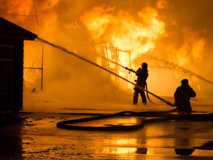 Firefighters extinguishing large flames at night with hoses.